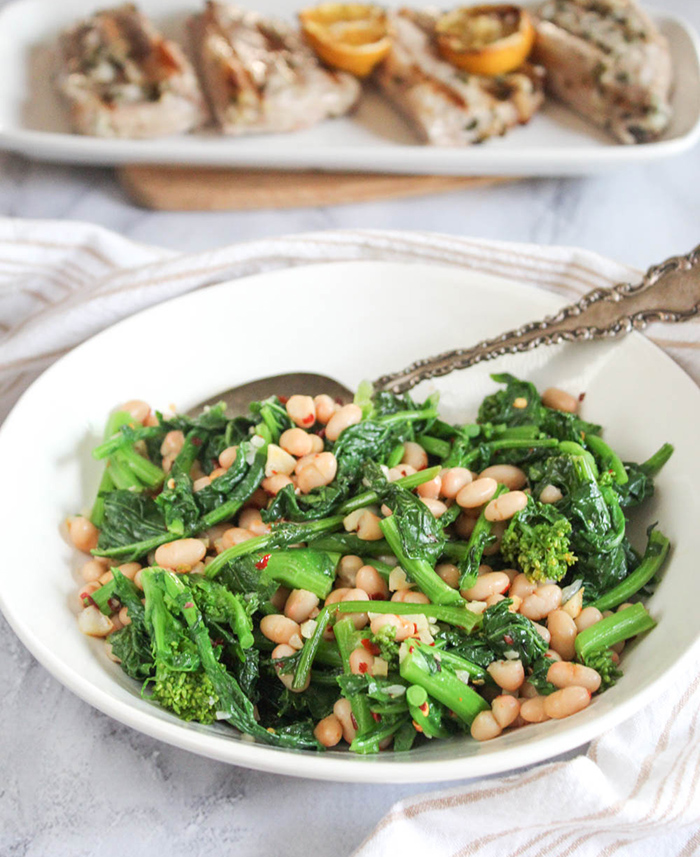 sauteed broccoli rabe with white beans in a white bowl with a serving spoon