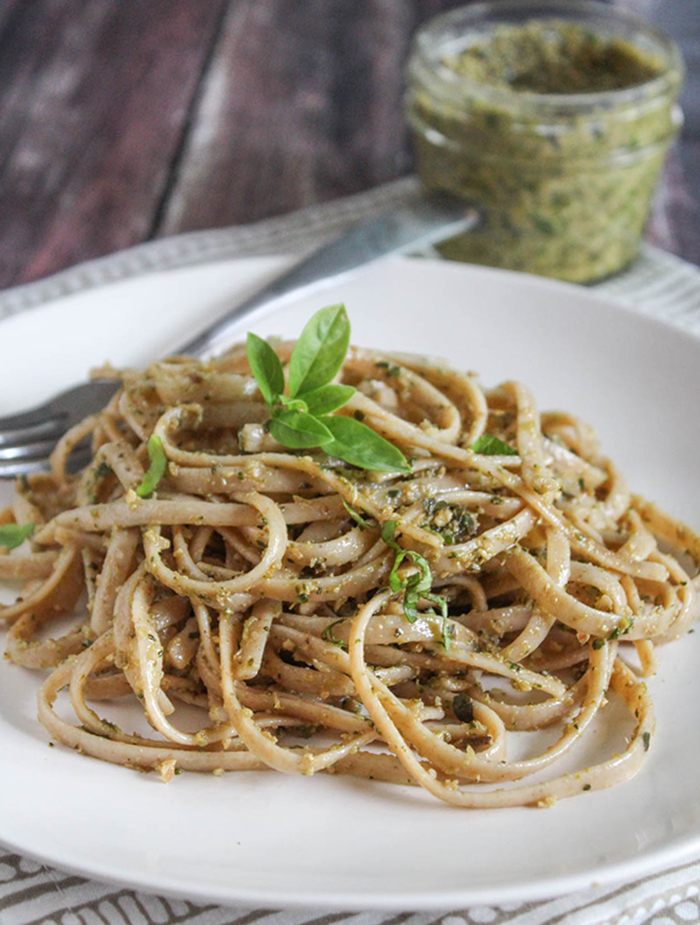 pasta on a plate with a jar of pesto in the background