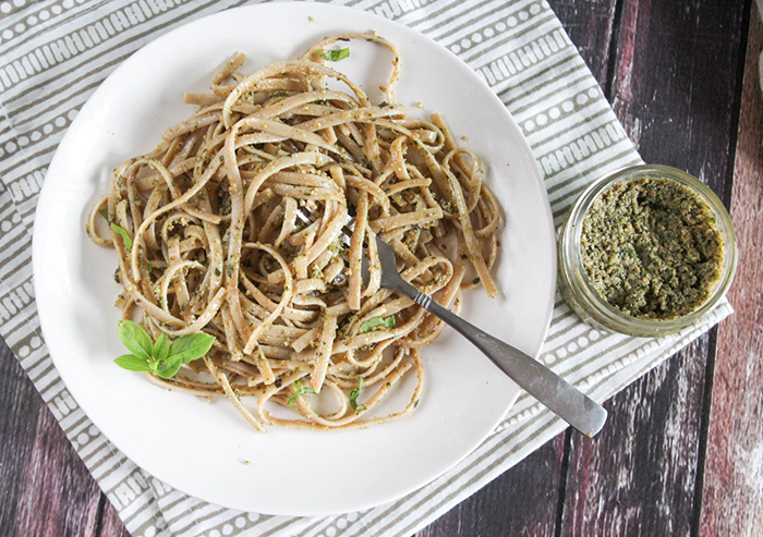 an overhead view of pasta on a plate with a jar of pesto on the side