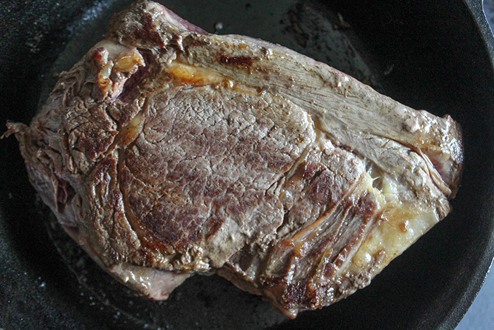 A picture of chuck roast cooking in a pan