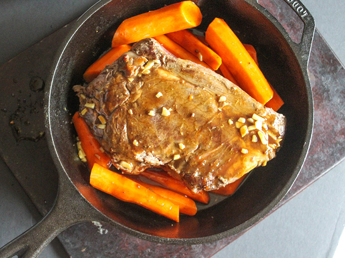 A picture of chuck roast cooking in a pan with carrots and sauce