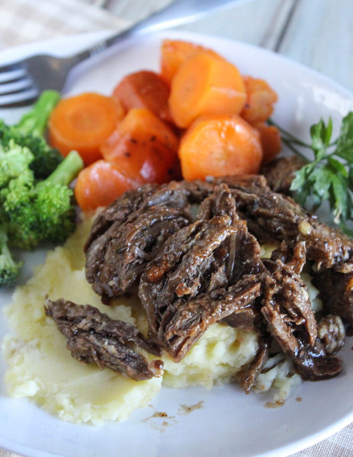 shredded beef pot roast covered in sauce with carrots and broccoli on the side