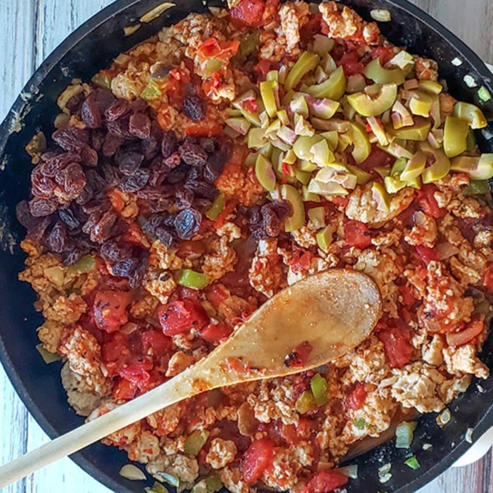 a picture of olives and raisins added to the picadillo skillet