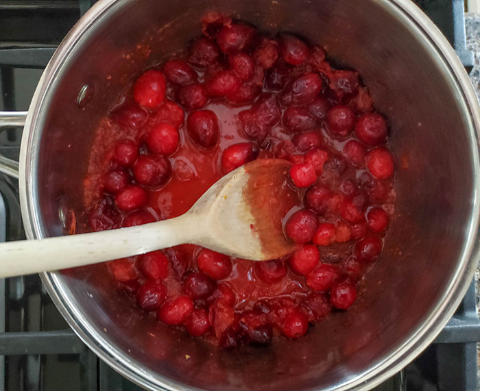 cranberries and juice cooking in a pan with a wooden spoon