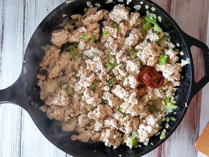 ground chicken cooking in a skillet with adobo sauce and spices