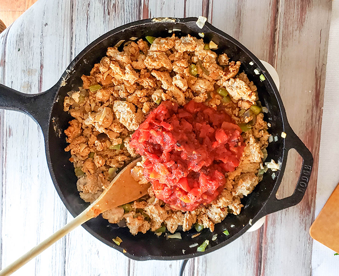 chicken cooking in a pan with tomatoes being added