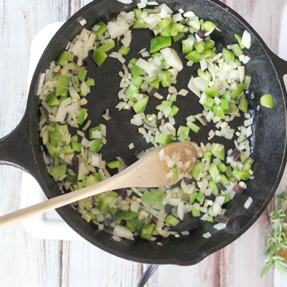 a picture of aromatics cooking in a cast iron skillet with a wooden spoon