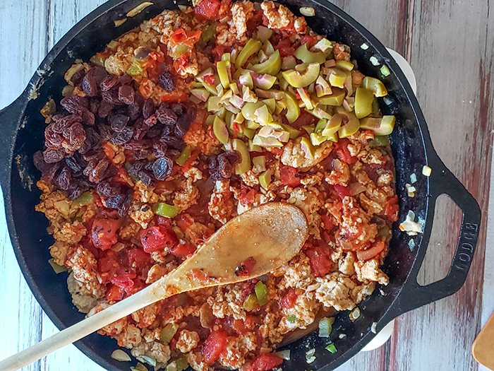 overhead view of picadillo cooking wit the addition of olives and raisins