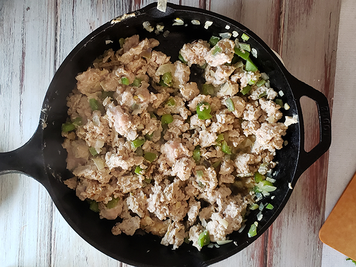 chicken cooking in a skillet with peppers and onions