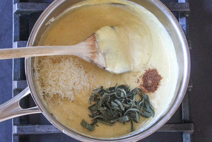 THe cream sauce with chopped sage nutmeg and cheese in a pan with a spoon