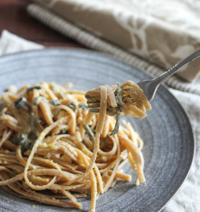 A close up picture of linguine on a fork with a blue plate of linguine in the back