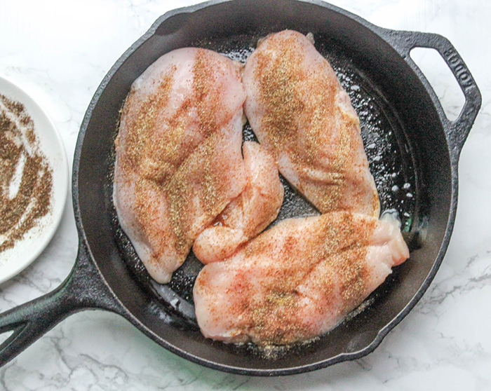 a picture of chicken cooking in a skillet with seasoning on top