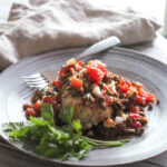 chicken breast on a plate covered with tomatoes, and chorizo sausage