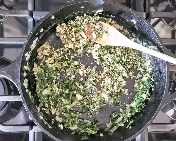 spinach onions and spices cooking in a skillet