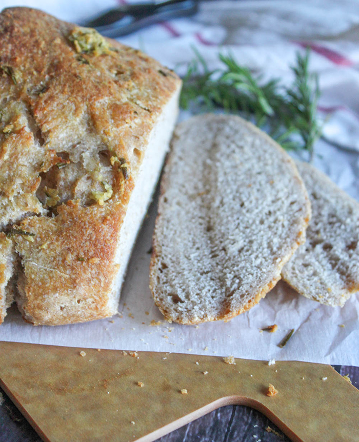 Sourdough bread sliced on a cutting board with fresh rosemary springs in the background