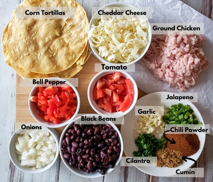 the ingredients on a cutting board: onions, bell pepper, corn tortillas, cheddar cheese, ground chicken, tomato, jalapeno, chili powder, cumin, cilantro, garlic