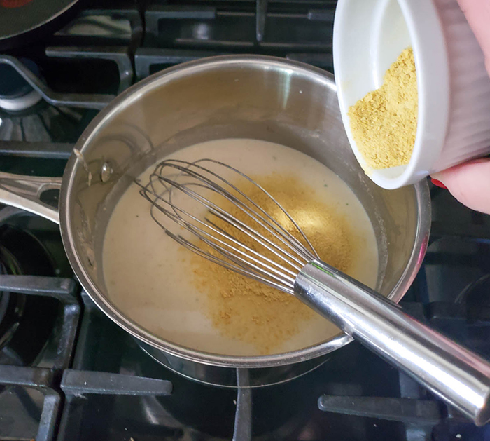 sauce in skillet with nutritional yeast being added