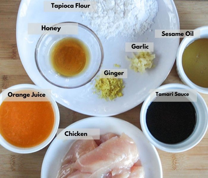 the ingredietns on a board: Clockwise: orange juice, honey, tapicoa flour, sesame oil garlic ginger, tamari sauce, chicken tenders