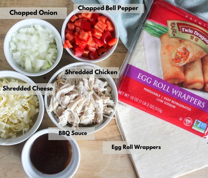  The ingredients on a cutting board: BBQ sauce, cheese, chicken, peppers, onions, egg roll wrappers