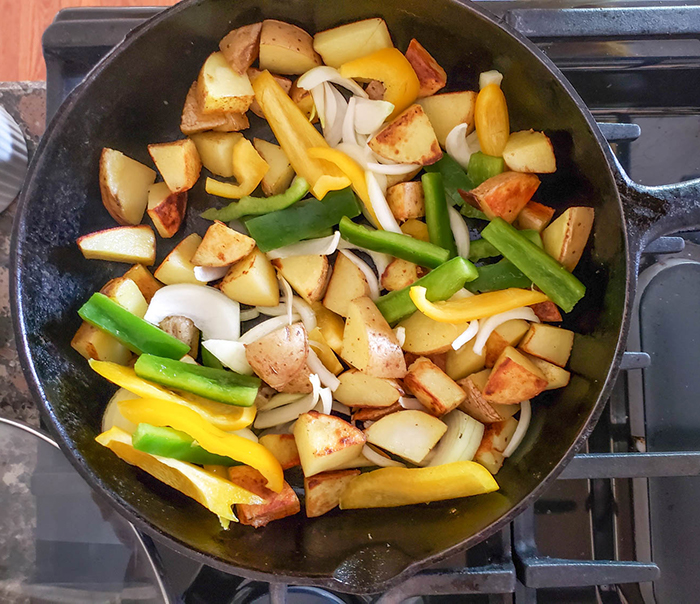 an overhead shot of potatoes cooking with peppers and onions in a skillet