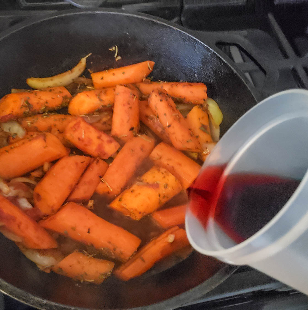 carrots and onions in a skillet with wine pouring in