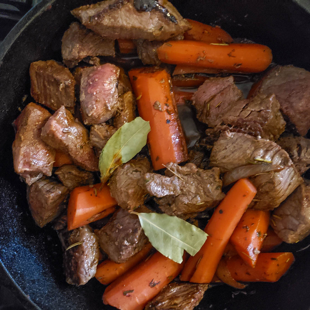 an overhead view of stew (beef, carrots, bay leaves) in a skillet ready to put in the oven