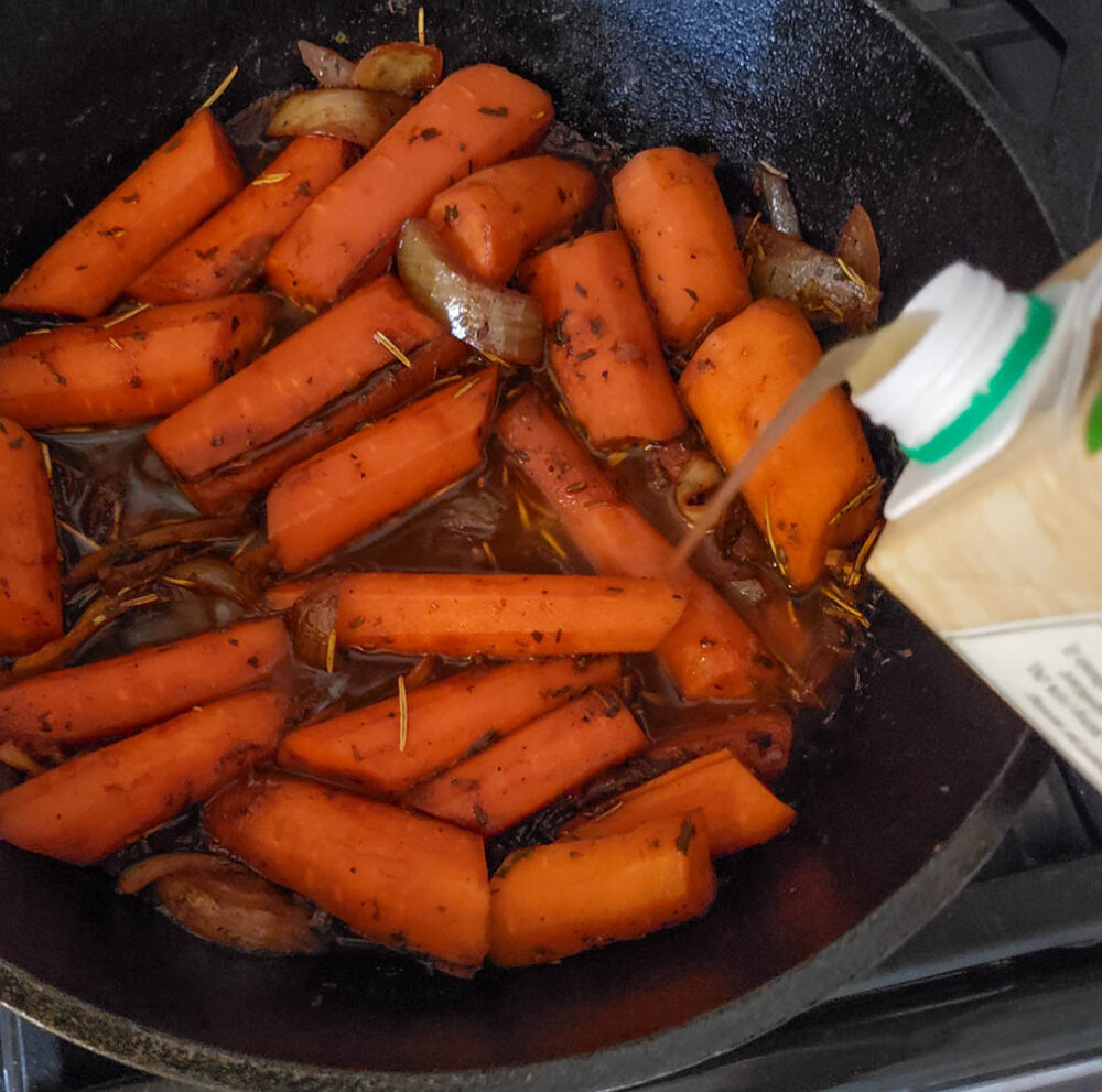 Carrots cooking in a skillet with broth pouring in