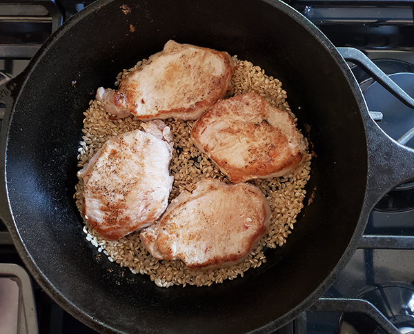 pork chops on top of raw rice in a cast iron skillet