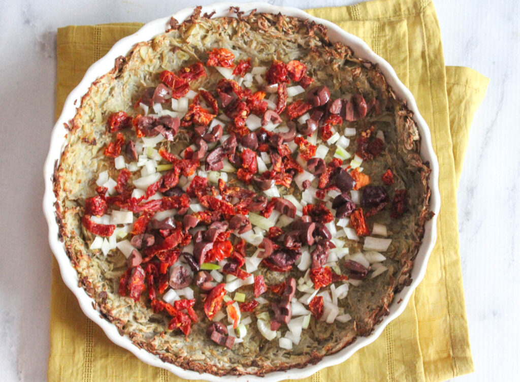 an overhead view of sun-dried tomatoes olives and onions on top of the potato crust