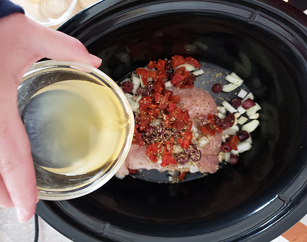 pouring broth onto the chicken with tomatoes, onions olives 