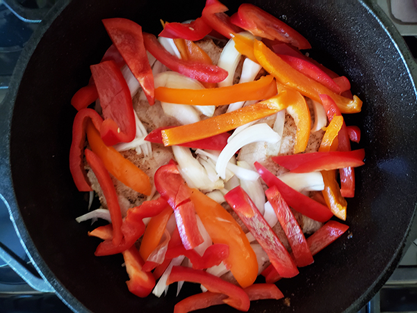 pork chops in a skillet topped with sliced peppers and onions;