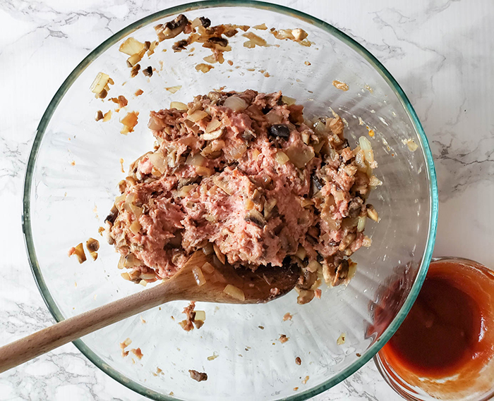 This is a picture showing step three of the recipe where you gently stir all ingredients. The image shows a spoon, glass mixing bowl and ingredients of turkey, mushroom mixture, tamari and Worcestshire.