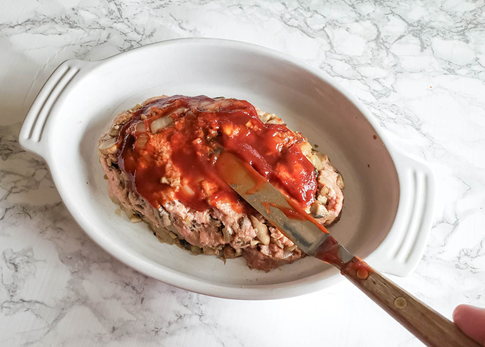 turkey meatloaf in a baking dish with a knife spreading on the glaze