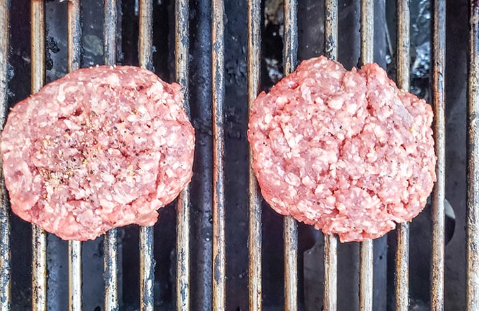 a picture of two beef burgers cooking on a grill
