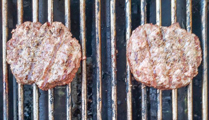 two beef burgers on a grill cooked