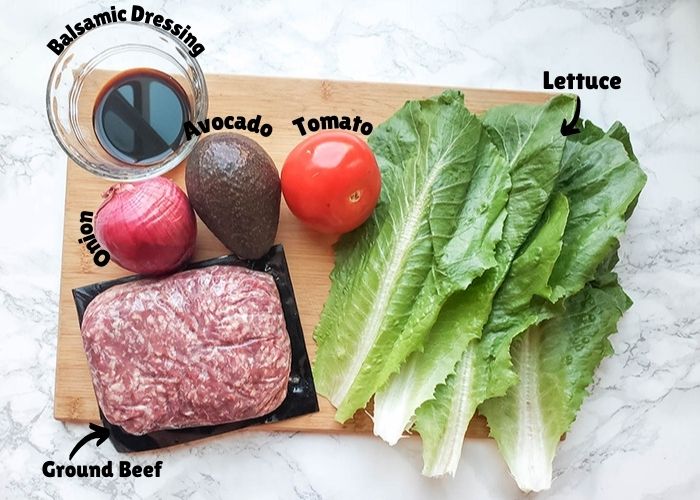 This image shows ingredients for burger bowls. In the picture are lettuce, tomato, avocado, red onion, ground beef and balsamic dressing.