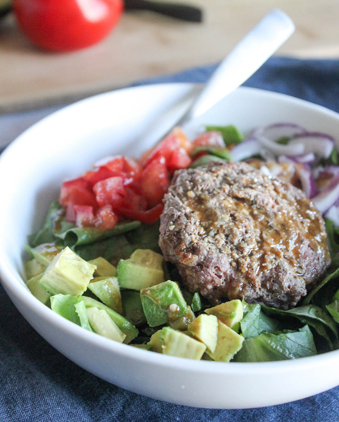 a close up picture of a burger bowl with lettuce, burger, tomatoes chopped avocaods