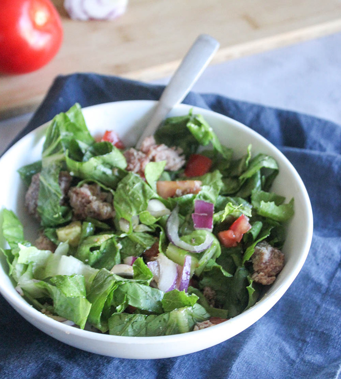 a bowl of lettuce, chopped up hamburger, onions avocado and tomatoes