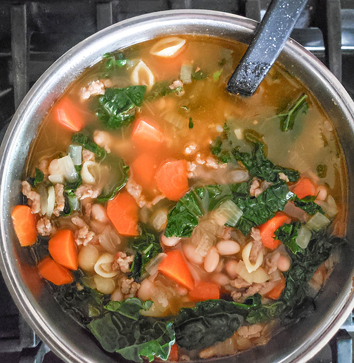 A pot of soup with wilted kale and cooked carrots