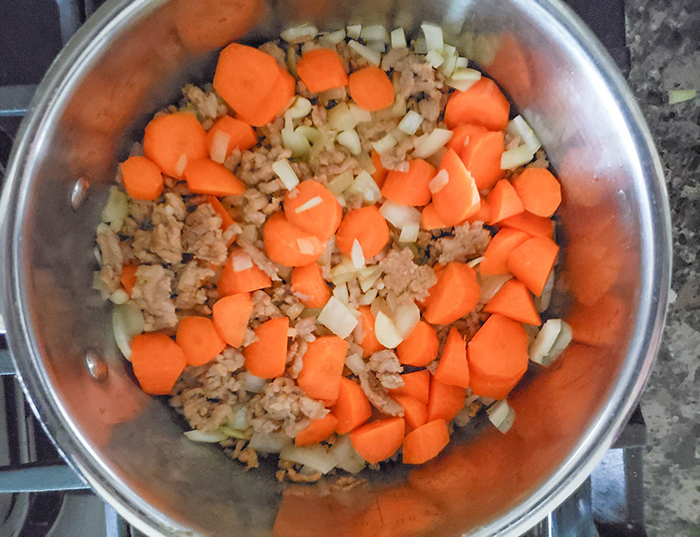 an overhead view of carrots, sausage and onions cooking in a pot