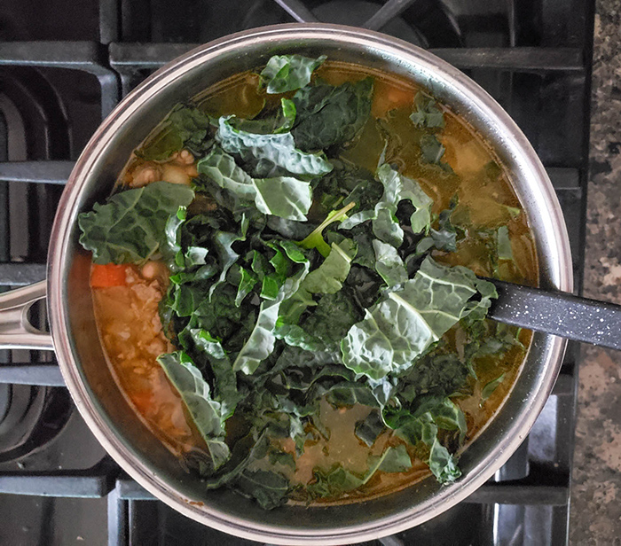 A pot of soup with uncooked kale on top