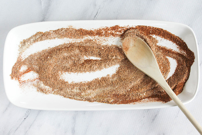 spices mixed together on a white plate with a wooden spoon