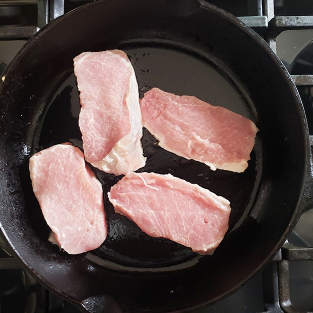 uncooked boneless pork chops in a skillet cooking