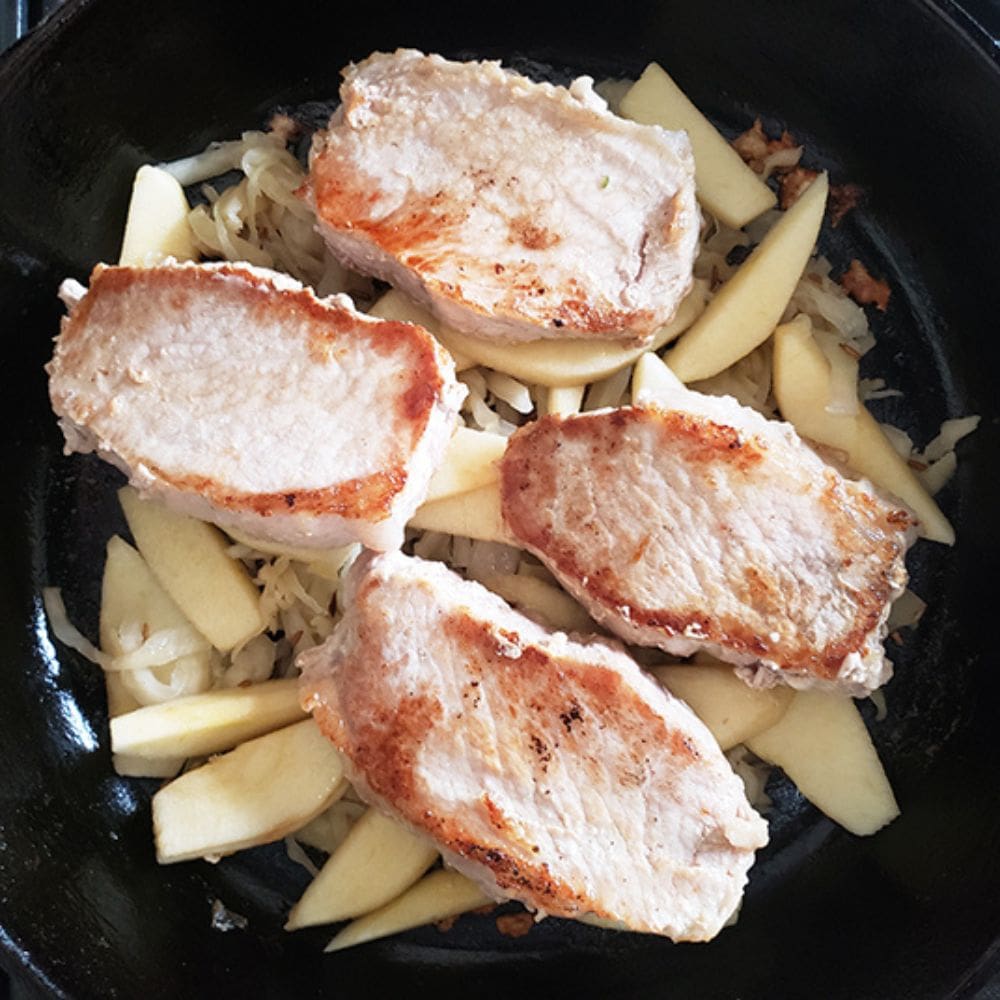 process 5 golden brown boneless chops on top of apples and sauerkraut in a skillet ready for teh oven