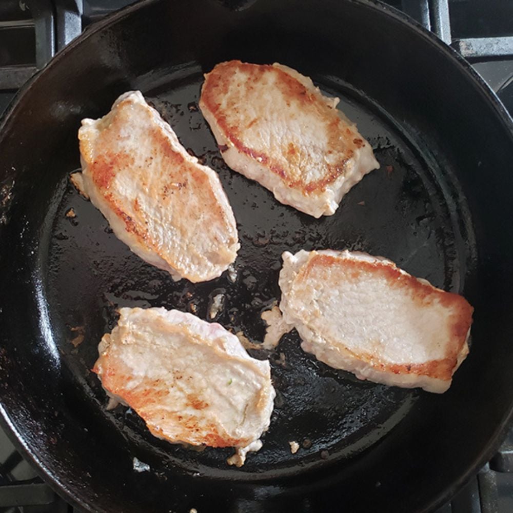 process step 2 boneless pork chops searing in a skillet with a golden brown exterior