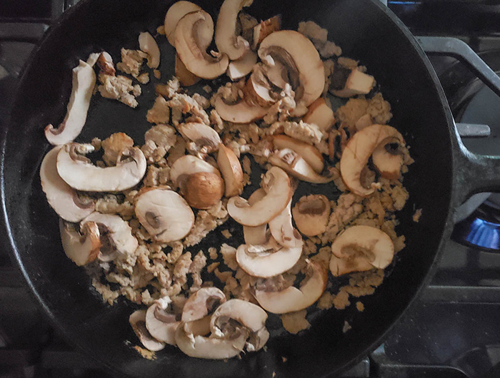 Mushrooms cooking with the ground pork in a skillet