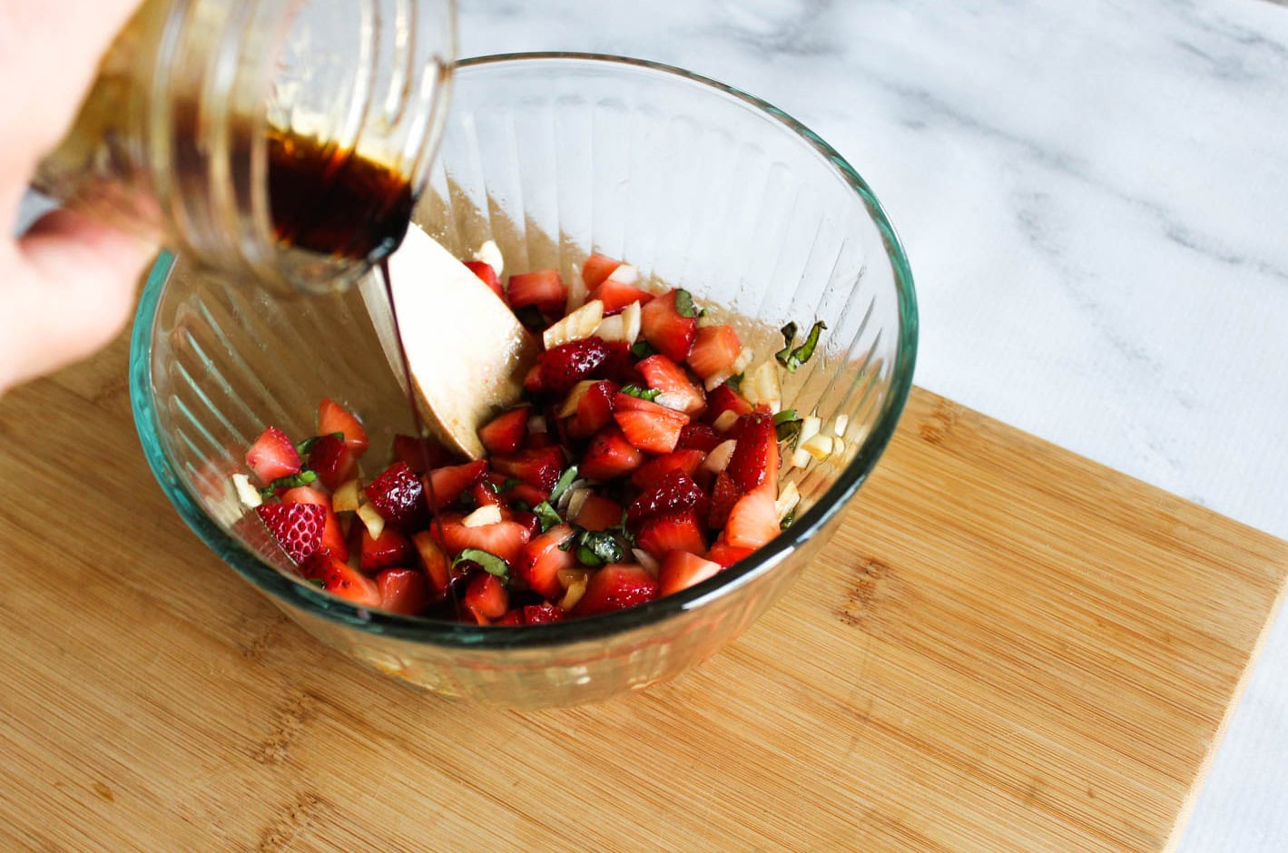 salsa ingredients in a glass bowl with balsamic dressing pouring in
