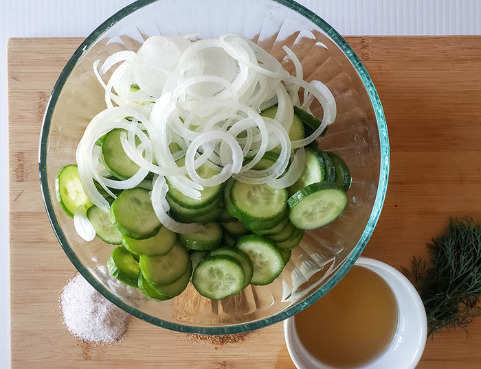 cucumber slices and onions slices in a bowl with vinegar on the side
