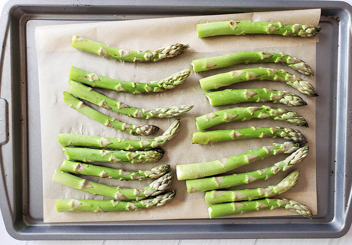 Raw asparagus arranged on a parchment lined baking sheet