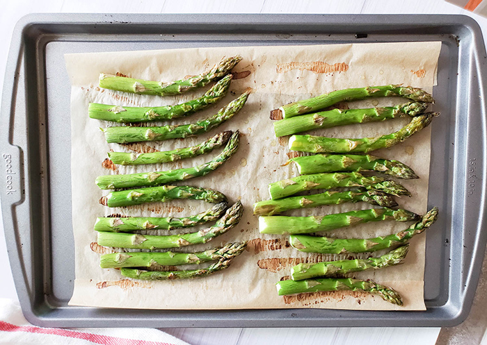 roasted asparagus arranged on a baking sheet with oil